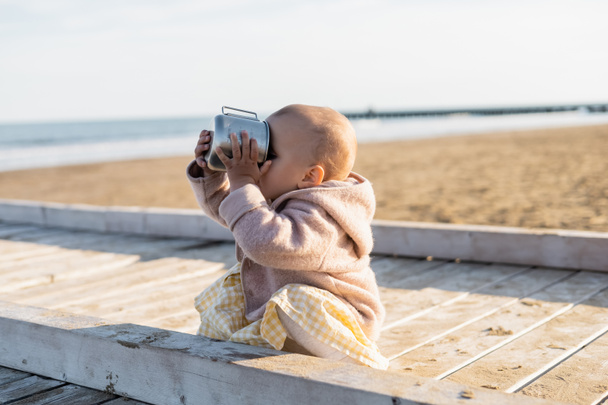 Baby girl drinking from cup on beach in Italy  - Фото, зображення