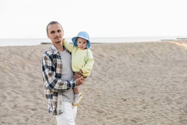 Mladý muž v košili drží dceru v panamě klobouk na pláži  - Fotografie, Obrázek
