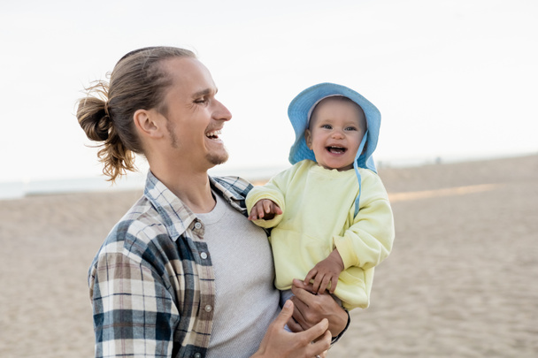Joyeux papa regardant fille en chapeau panama sur la plage  - Photo, image