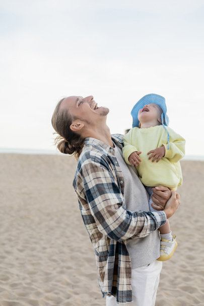 Young man and toddler daughter laughing on beach  - Фото, изображение