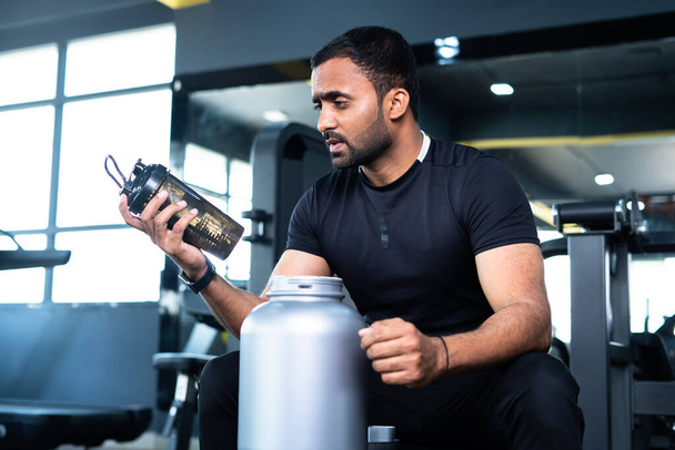 bodybuilder drinking protein by shaking bottle after gym workout session - concept of weight loss, muscle building and nutrition supplement - Photo, image