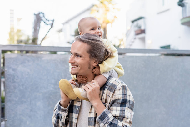 笑顔の赤ん坊はトレヴィーゾの都会の通りで若い父親の肩に座っている - 写真・画像