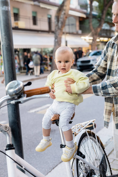 Genitore sorridente che tiene in braccio la bimba vicino alla bici sulla strada urbana di Treviso - Foto, immagini