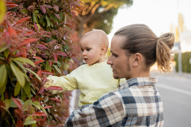 Homme tenant bébé fille près de la plante en plein air  - Photo, image