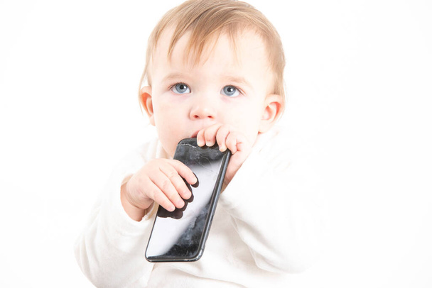 Foto de estudio en stock con el fondo blanco de la cara de un bebé con un móvil en la boca
 - Foto, imagen