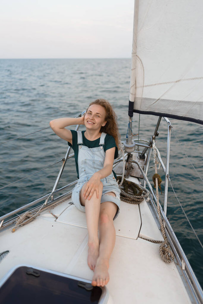 若い美しい赤毛の女性が海のヨットのデッキに横たわっています。女は水の上で休んでいる - 写真・画像