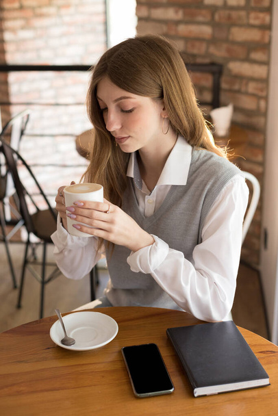 girl blogger drinks cappuccino in a coffee shop in the morning - Foto, afbeelding
