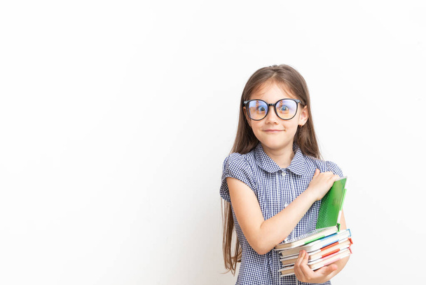 Een 7-jarig meisje met een bril met boeken met een verrassend gezicht. Onderwijs voor kinderen, leerconcept met kopieerruimte. - Foto, afbeelding