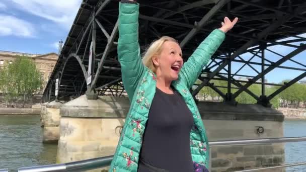 een volwassen vrouw in een groen jasje zwemt onder een brug in Parijs en schreeuwt juichend zwaaiend met haar armen omhoog video slow motion ze heeft veel geluk en vreugde - Video
