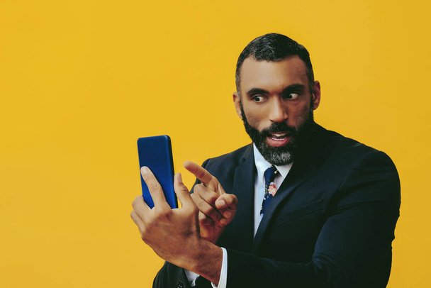 portrait of handsome bearded man in suit with smartphone and mobile phone on yellow background - Foto, Imagen