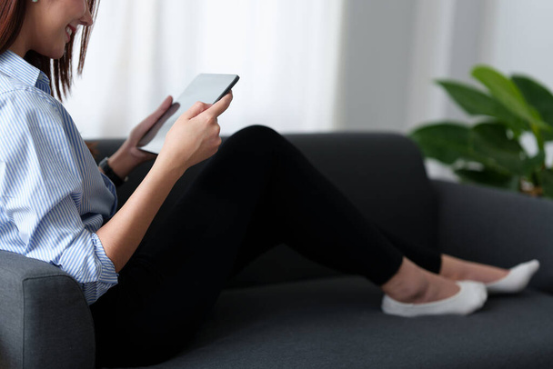 Женщина наслаждаться контентом потокового фильмов или приложений социальных медиа на цифровой планшет сидя рядом диван дома. - Фото, изображение