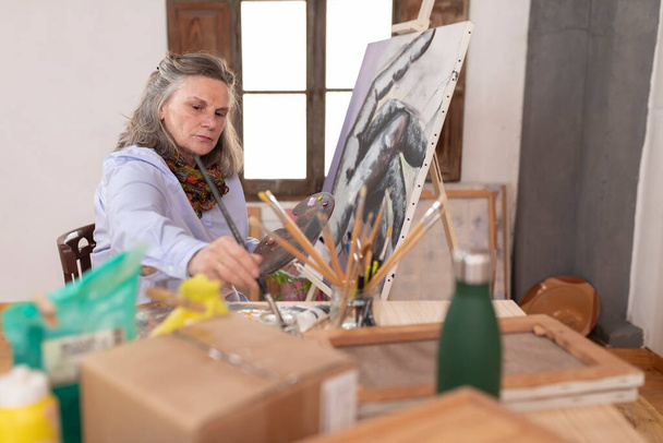 Зрелая художница чистит кисть перед тем, как использовать другой цвет в мастерской - Фото, изображение