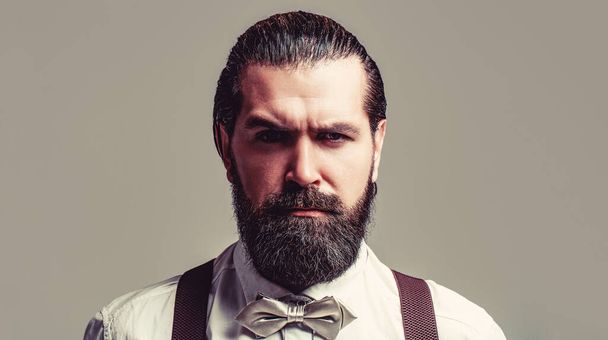 Portrait of handsome bearded man in white shirt and bow tie, suspenders. Close-up of a gentleman his bowtie. Beard man in bow tie and suspenders. Male in shirt correcting his colorful tie - Фото, изображение