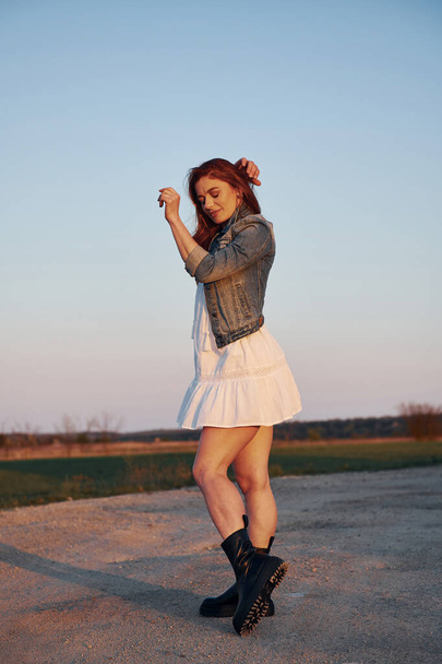 Redhead woman in skirt standing and posing for a camera on the road at evening time. - Fotoğraf, Görsel