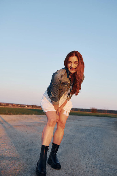 Redhead woman in skirt standing and posing for a camera on the road at evening time. - Foto, afbeelding