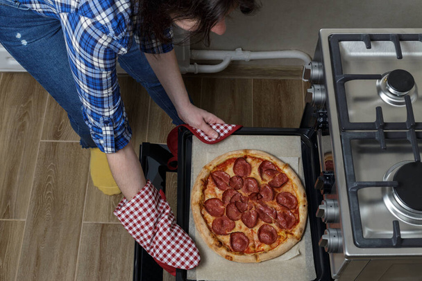 Dziewczyna wyjmuje pizzę z piekarnika. domowej roboty pizza pepperoni - Zdjęcie, obraz