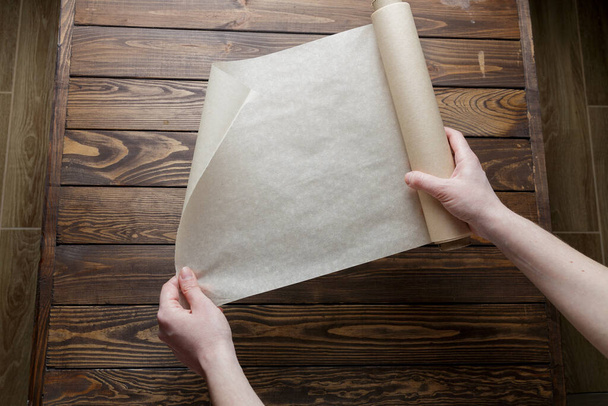 бумага для выпечки на деревянном фоне. девочка разворачивает рулон пекарской бумаги. - Фото, изображение