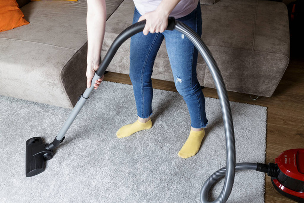 a girl in blue jeans vacuums the carpet. House cleaning. - Foto, Bild