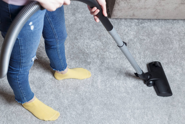 a girl in blue jeans vacuums the carpet. House cleaning. - Fotografie, Obrázek