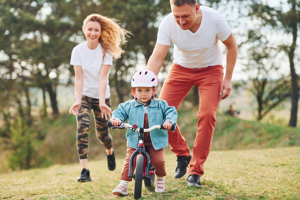 Mother and father teaching daughter how to ride bicycle outdoors. - Foto, Imagem