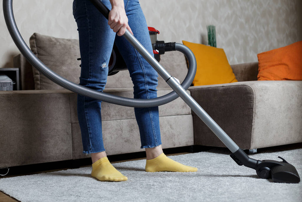 a close-up photo of the legs of a girl with a vacuum cleaner in her hands. girl cleans the house. - Foto, Bild