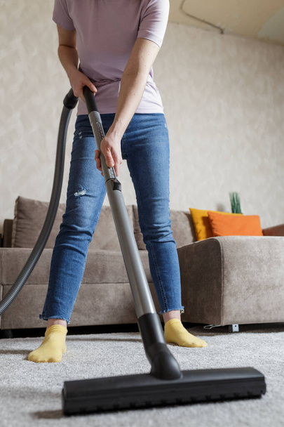 house cleaning concept. a close-up photo of a girl's legs and a vacuum cleaner brush. the girl cleans the house and vacuums the carpet. - Photo, image