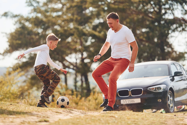 Playing soccer. Father with his son spending weekend together outdoors near forest at daytime. - 写真・画像