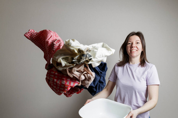 laundry washing concept. beautiful girl in a good mood, smiling, throwing up a lot of dirty clothes, has a happy look, has fun - Foto, Bild