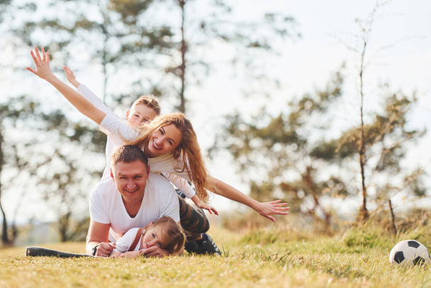 Sitting and lying on the ground. Happy family spending weekend together outdoors near the forest. With daughter and son. - Foto, imagen