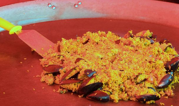 large pan with spanish paella with rice seafood and mussels under the RED infrared lamp to keep the heat of the dish at street food stand market - Φωτογραφία, εικόνα