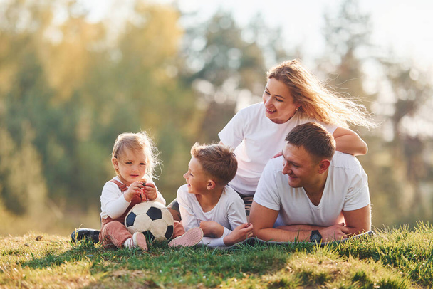 With soccer ball. Happy family lying down outdoors near the forest. With daughter and son. - 写真・画像