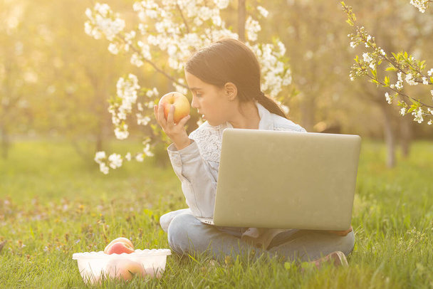 裏庭でノートパソコンを使う少女。家庭で勉強している子供は宿題をしたり、オンラインレッスンを受けたりします。家庭教育の概念. - 写真・画像