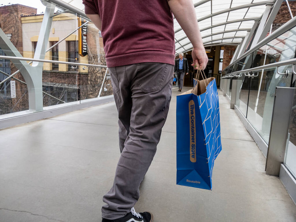 Bellevue, WA USA - circa April 2022: Low angle view of a man walking with a bag from The Container Store while wandering the Bellevue Mall - Photo, image