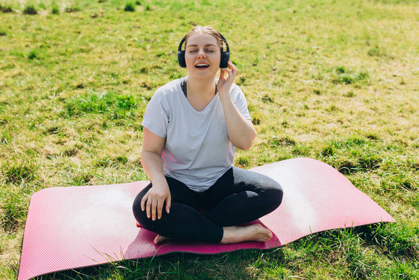 Beautiful young redhead woman relaxing on Yoga Mat after Training. Happy girl with Earphones Listening Music. Sport or yoga concept - Valokuva, kuva
