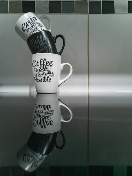 Stack of black and white mugs with calligraphy writings on it standing on reflective black surface - 写真・画像
