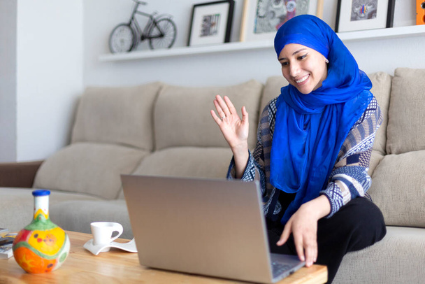 Улыбающаяся мусульманка делает видеоконференцию через ноутбук. Удаленные отношения. Пространство для текста. - Фото, изображение