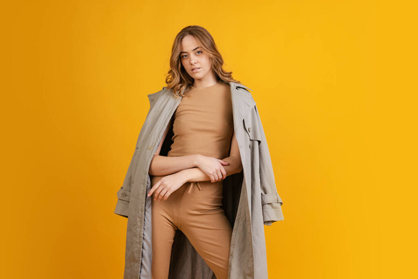 Emotional girl, student in costume and raincoat posing isolated on orange background. Concept of beauty, art, fashion, youth, monochrome - Foto, afbeelding