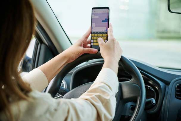 Auto rijden. Vrouwelijke bestuurder met mobiele telefoon een stuurwiel in een nieuwe auto. Selectieve focus, bijgesneden. Autoverzekeringsconcept. - Foto, afbeelding