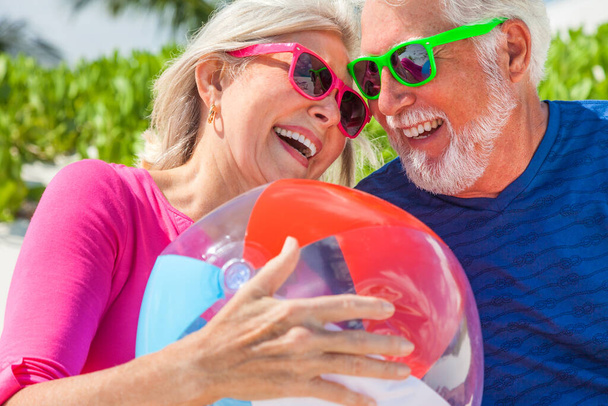 Attraktive männliche und weibliche kaukasische Senioren amüsieren sich gemeinsam in den Tropen mit bunter Sonnenbrille und Strandball  - Foto, Bild