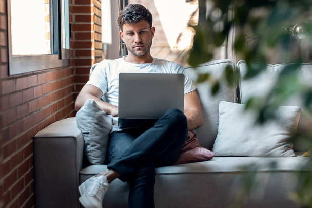 Shot of smart man working with her laptop while sitting on a couch at home - Photo, image