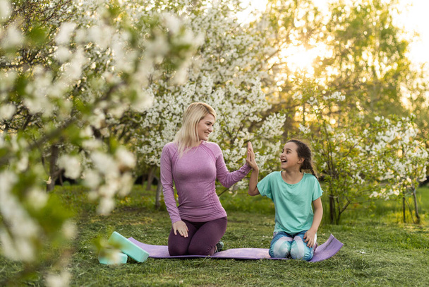 Young sports mother doing physics exercise outdoors in garden near her daughter. Healthy lifestyle. Yoga. Fitness. Family having fun outside. Family spend time together in park. - Foto, immagini