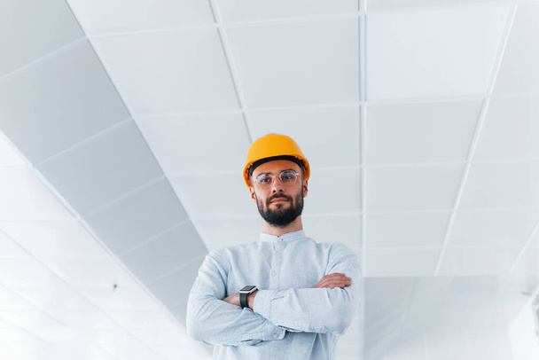 Portrait of engineer in white clothes and orange protective hard hat that standing and working indoors. - Fotoğraf, Görsel