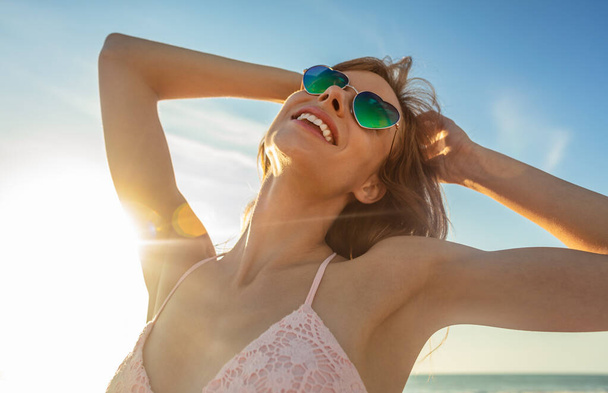 Carefree young American girl wearing sunglasses on beach at sunrise enjoying solo life on fun Summer vacation - Фото, зображення