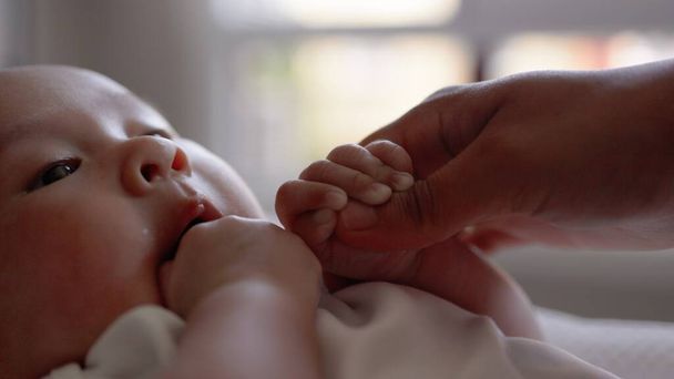 Beyazlı şirin bebek annesinin elini tutuyor ve parmağını emiyor.  - Fotoğraf, Görsel