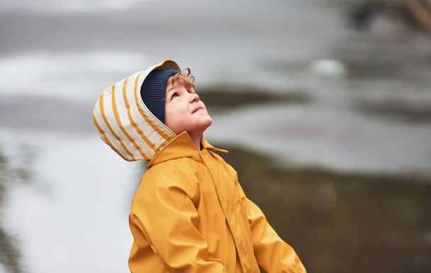 Kid in yellow waterproof cloak and boots playing outdoors after the rain. - Foto, immagini