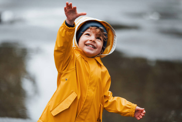 Kid in yellow waterproof cloak and boots playing outdoors after the rain. - Foto, immagini