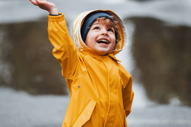 Kid in yellow waterproof cloak and boots playing outdoors after the rain. - Foto, Imagen