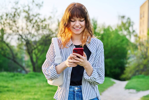 Outdoor portrait of trendy young red-haired girl with smartphone in hand - Zdjęcie, obraz