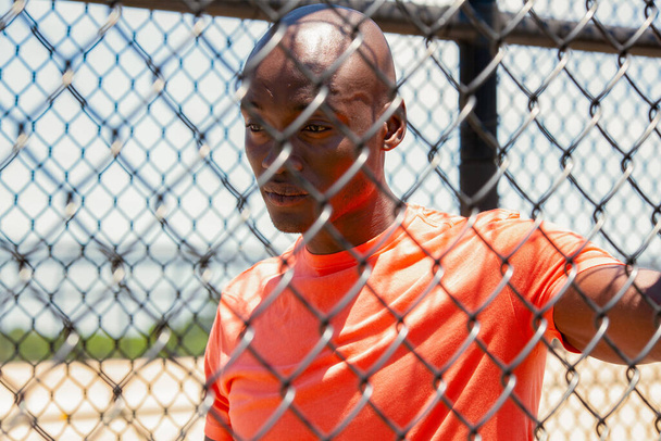Chain link fence walkway in suburban environment with healthy young Afro American male preparing for cardio workout - Photo, Image