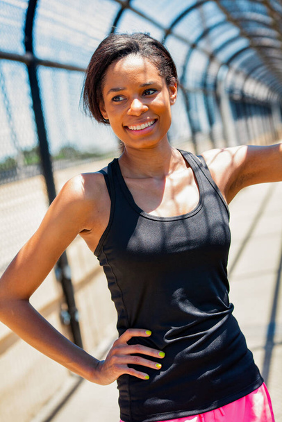 Fit junge Afroamerikanerin in Sportkleidung ruht auf überdachtem Gehweg beim gesunden Training in urbaner Umgebung - Foto, Bild